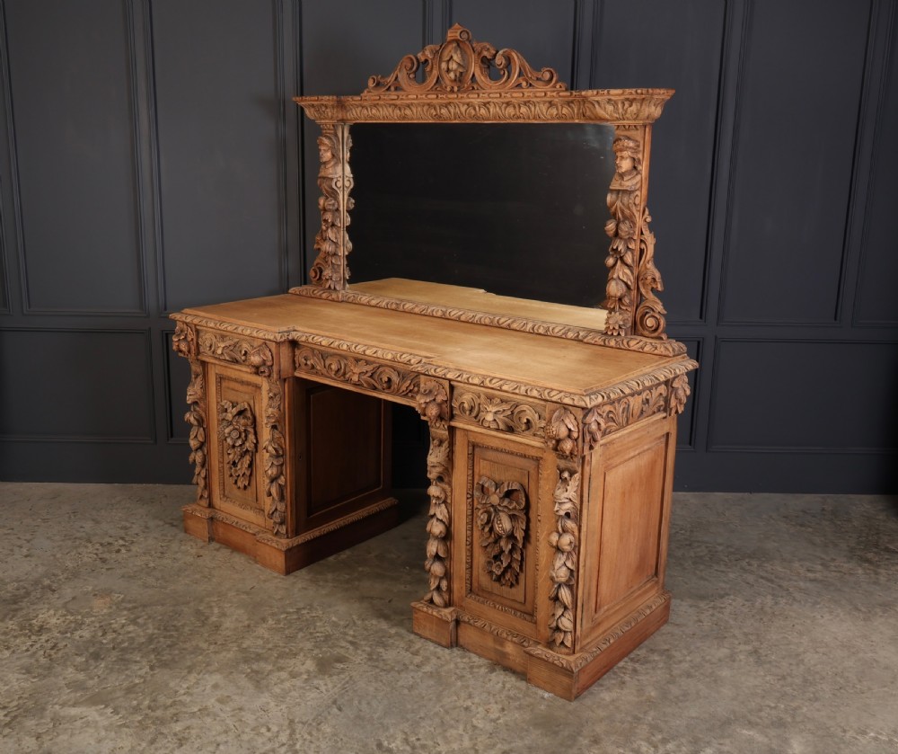 A large bleached oak pedestal sideboard featuring elaborate fruit swags, carved mask details, twin lower cupboards, and an integrated rectangular mirror superstructure. View V