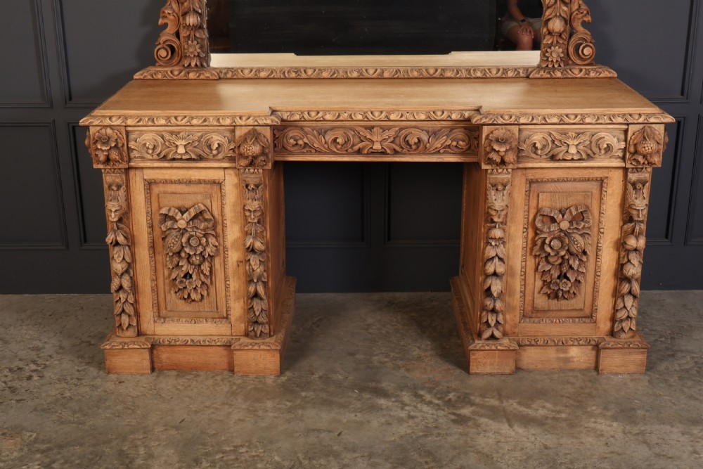 A large bleached oak pedestal sideboard featuring elaborate fruit swags, carved mask details, twin lower cupboards, and an integrated rectangular mirror superstructure. View VI