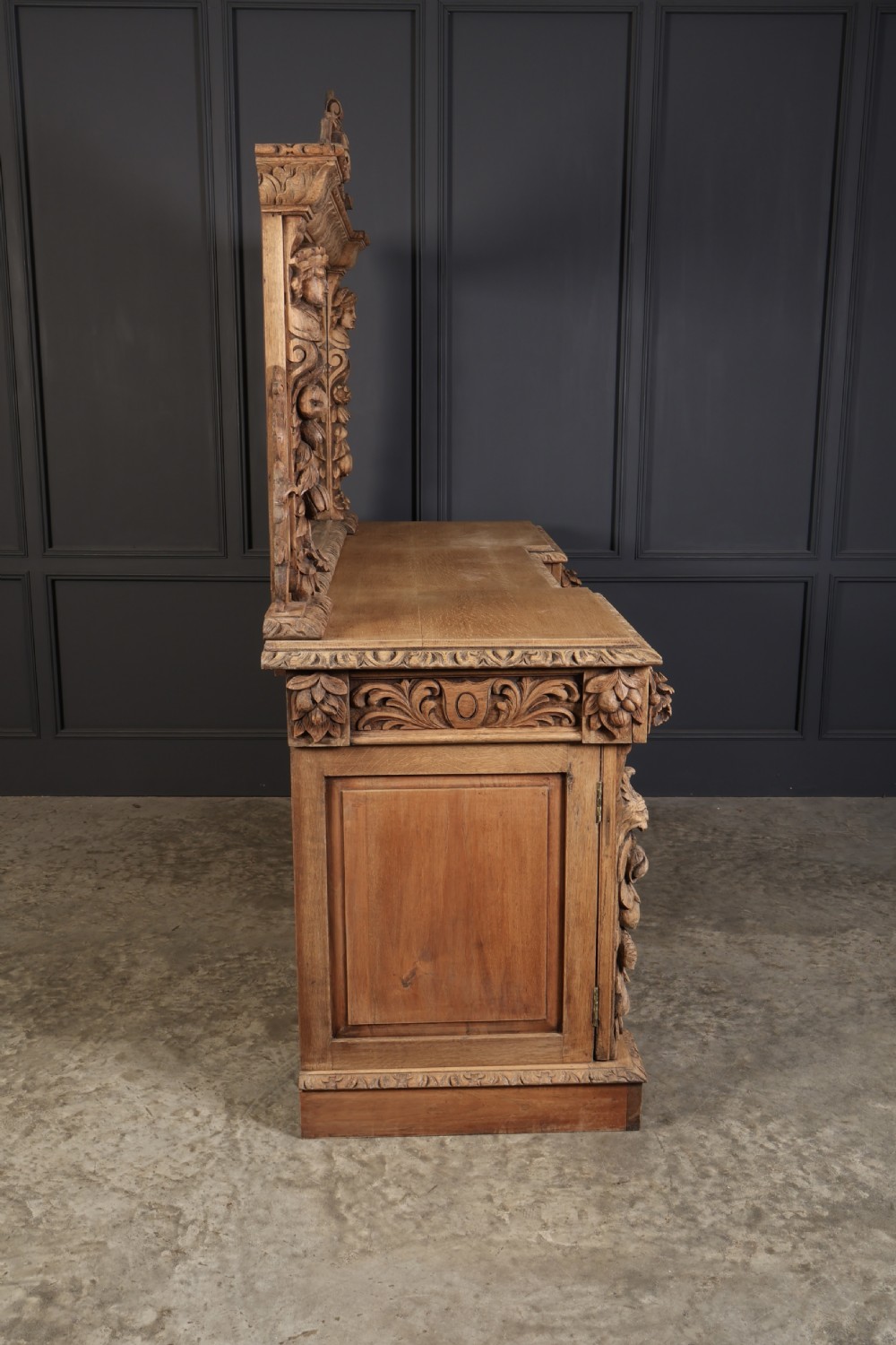 A large bleached oak pedestal sideboard featuring elaborate fruit swags, carved mask details, twin lower cupboards, and an integrated rectangular mirror superstructure. View IX