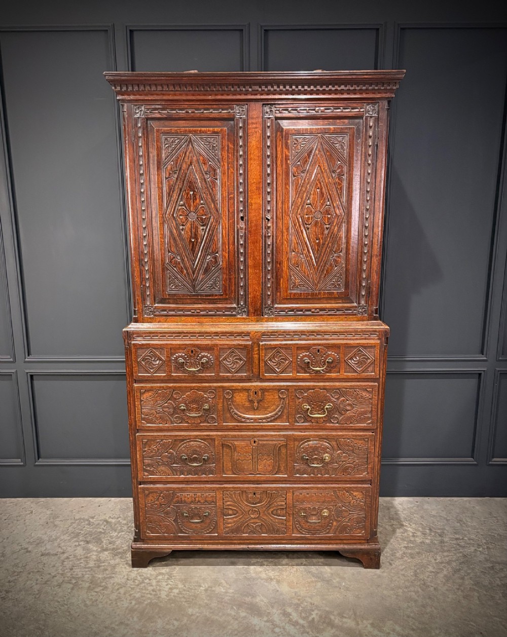 An 18th-century carved dark oak housekeepers cupboard featuring upper panel doors with geometric lozenge carving above a base with five carved drawers. View III