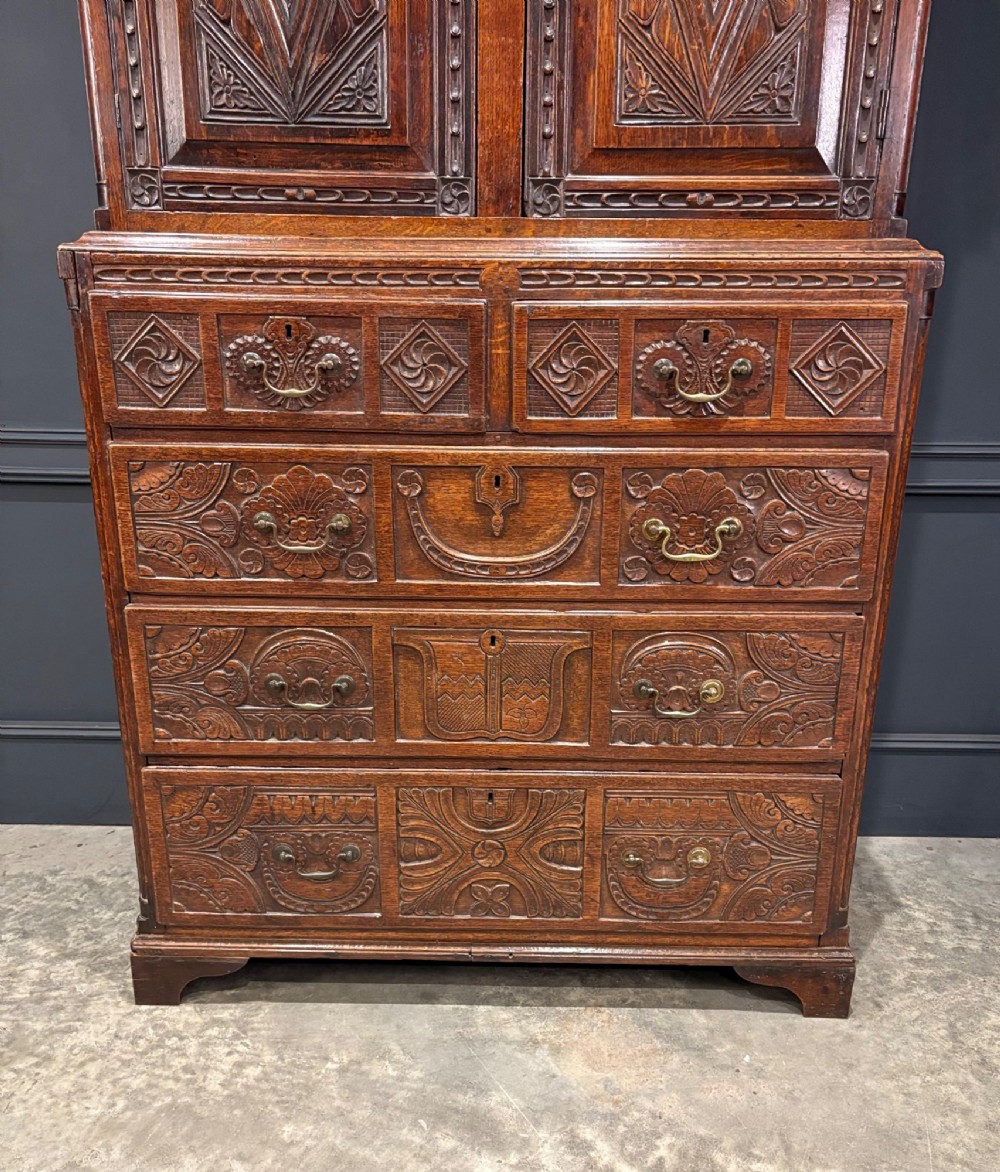 An 18th-century carved dark oak housekeepers cupboard featuring upper panel doors with geometric lozenge carving above a base with five carved drawers. View IV