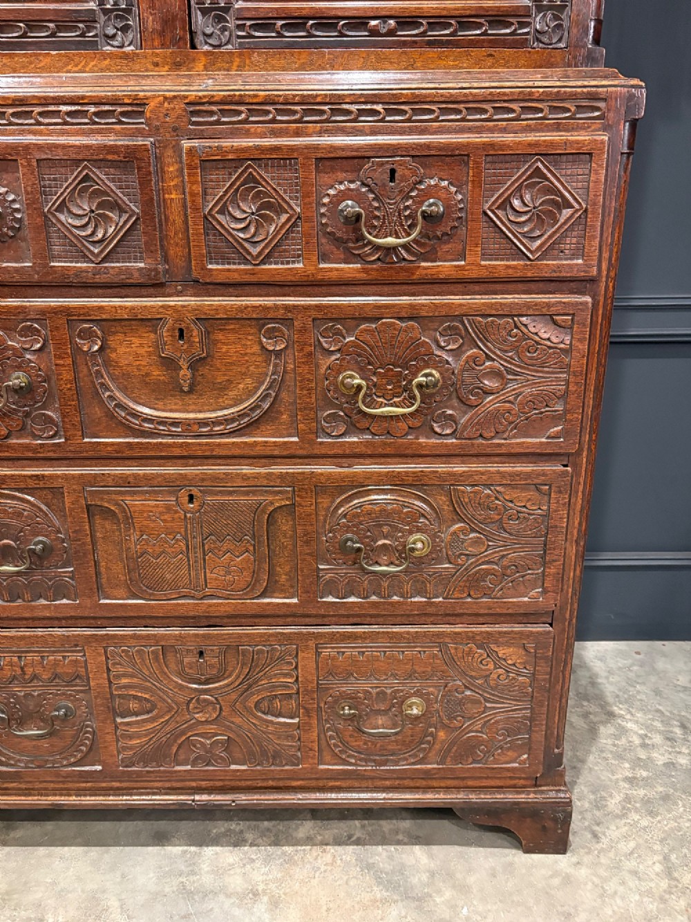 An 18th-century carved dark oak housekeepers cupboard featuring upper panel doors with geometric lozenge carving above a base with five carved drawers. View V
