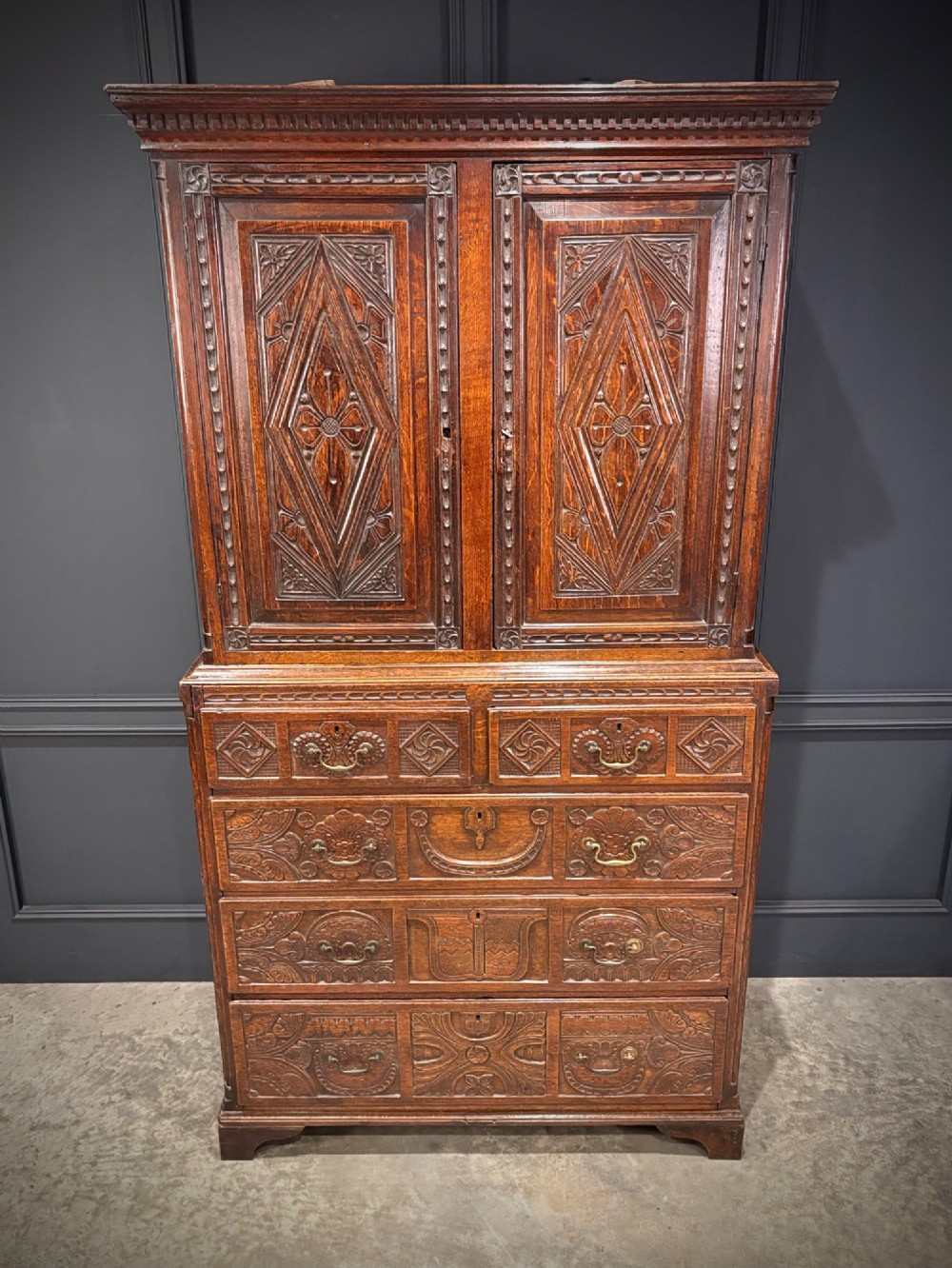 An 18th-century carved dark oak housekeepers cupboard featuring upper panel doors with geometric lozenge carving above a base with five carved drawers. View VI