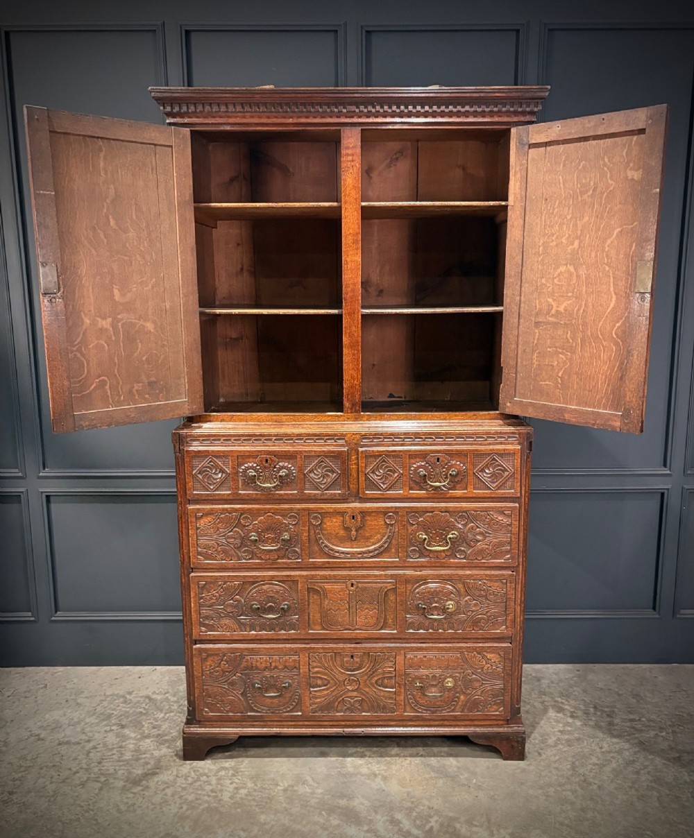 An 18th-century carved dark oak housekeepers cupboard featuring upper panel doors with geometric lozenge carving above a base with five carved drawers. View VII