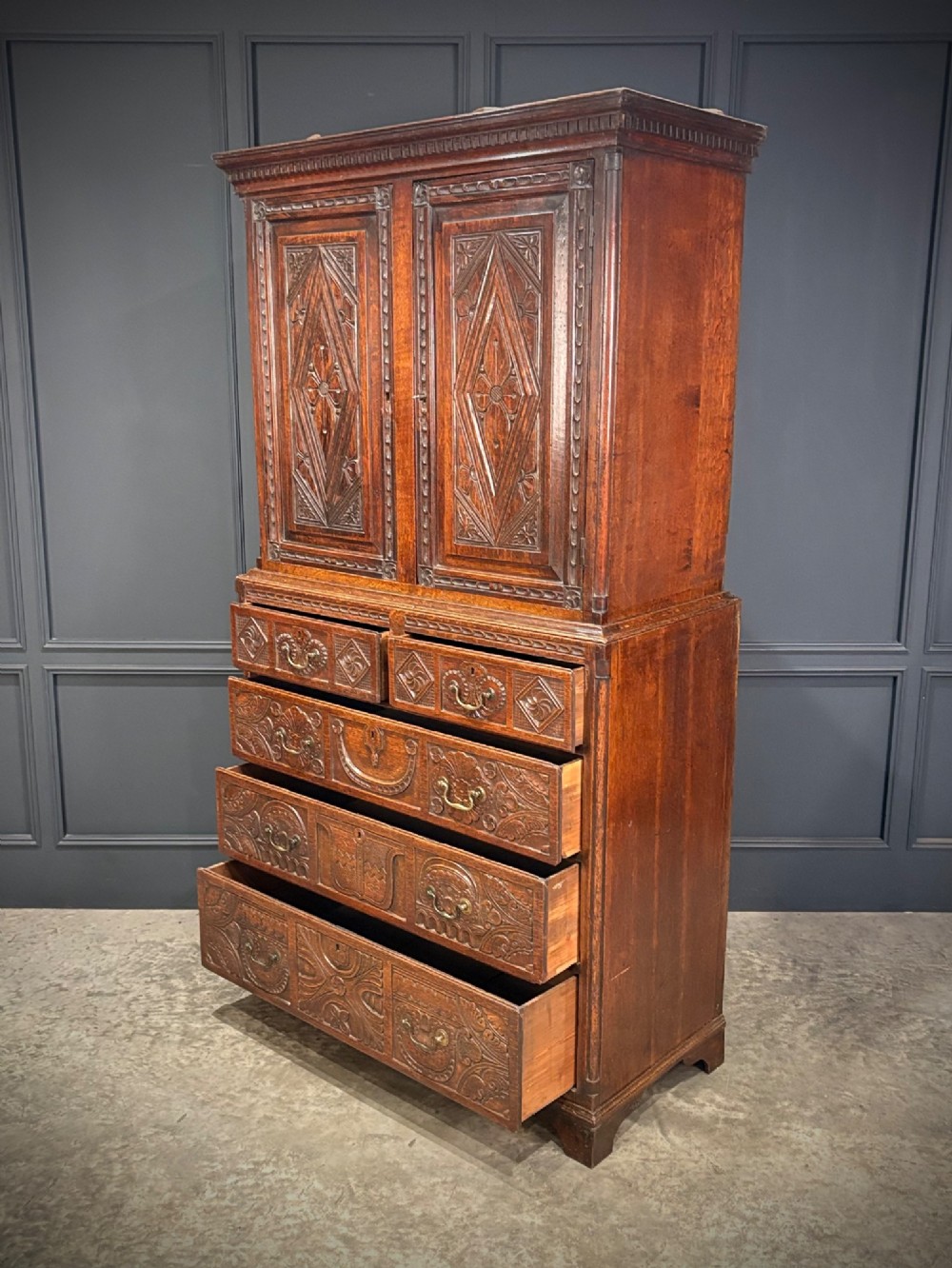 An 18th-century carved dark oak housekeepers cupboard featuring upper panel doors with geometric lozenge carving above a base with five carved drawers. View VIII