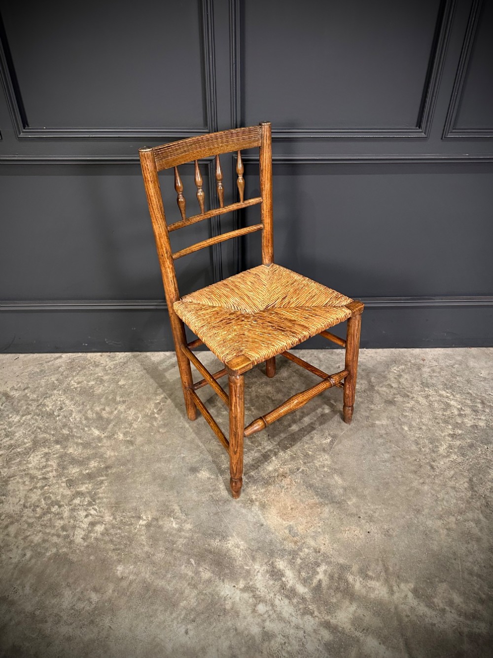 An 18th-century country elm side chair featuring a woven rush seat, turned spindle backrest, and turned wood legs connected by stretchers. View II