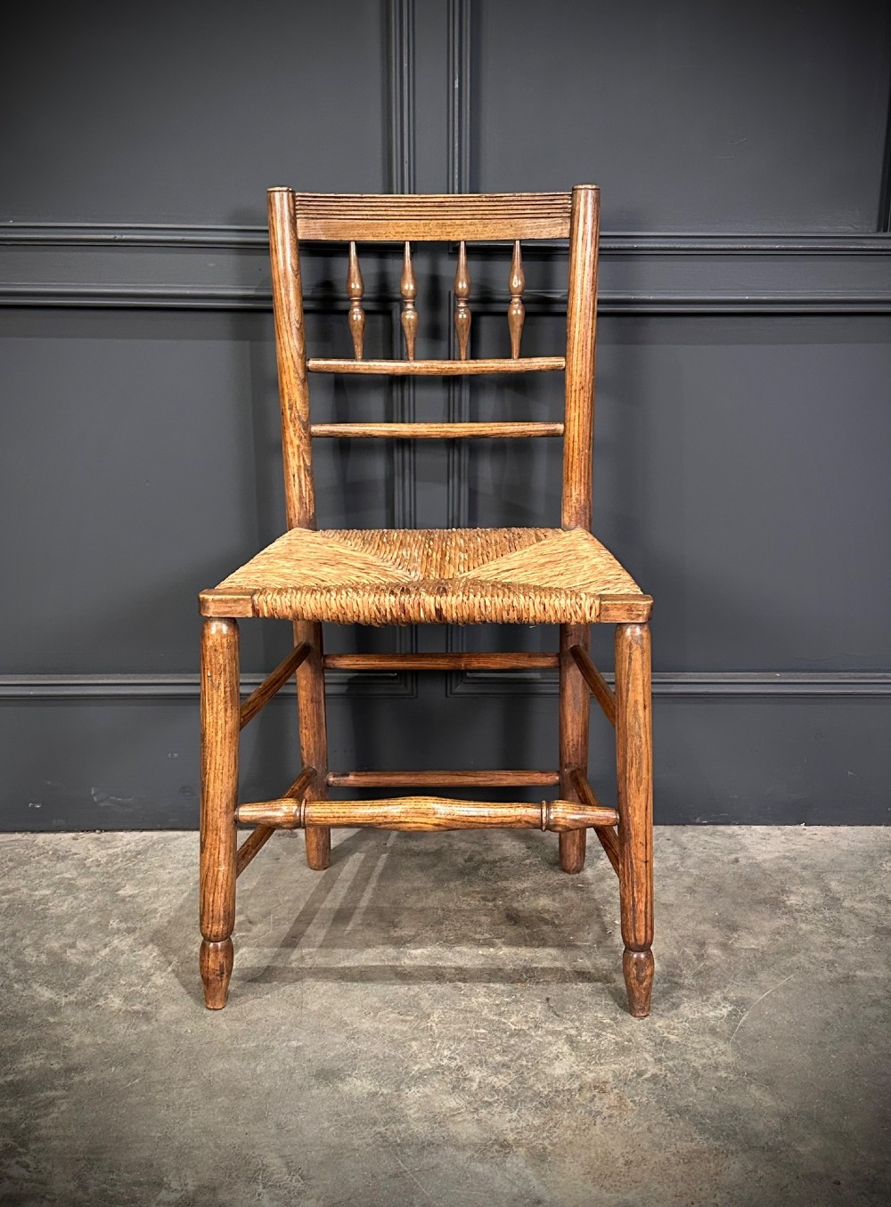An 18th-century country elm side chair featuring a woven rush seat, turned spindle backrest, and turned wood legs connected by stretchers. View III