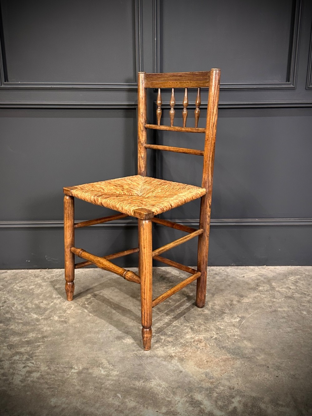 An 18th-century country elm side chair featuring a woven rush seat, turned spindle backrest, and turned wood legs connected by stretchers. View VI