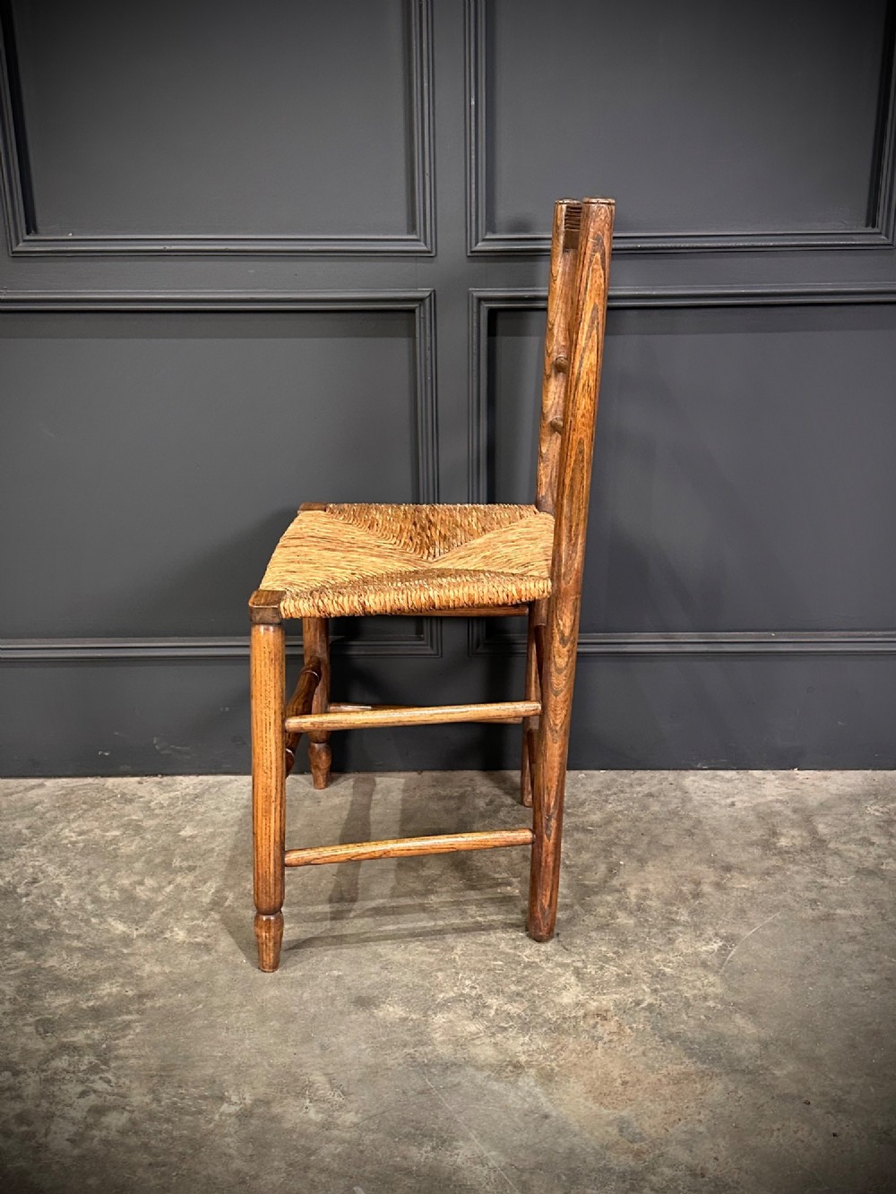 An 18th-century country elm side chair featuring a woven rush seat, turned spindle backrest, and turned wood legs connected by stretchers. View VII