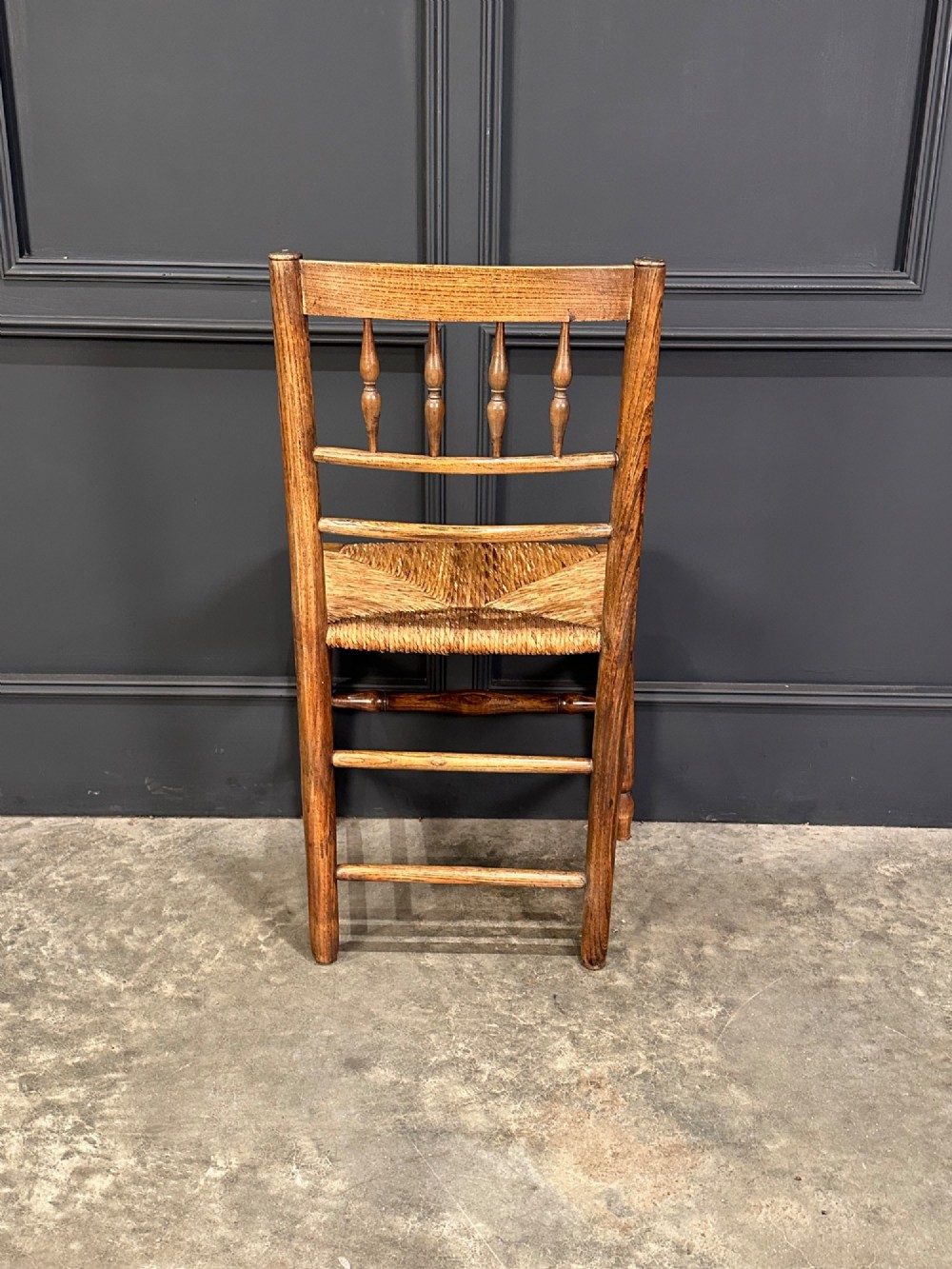 An 18th-century country elm side chair featuring a woven rush seat, turned spindle backrest, and turned wood legs connected by stretchers. View VIII