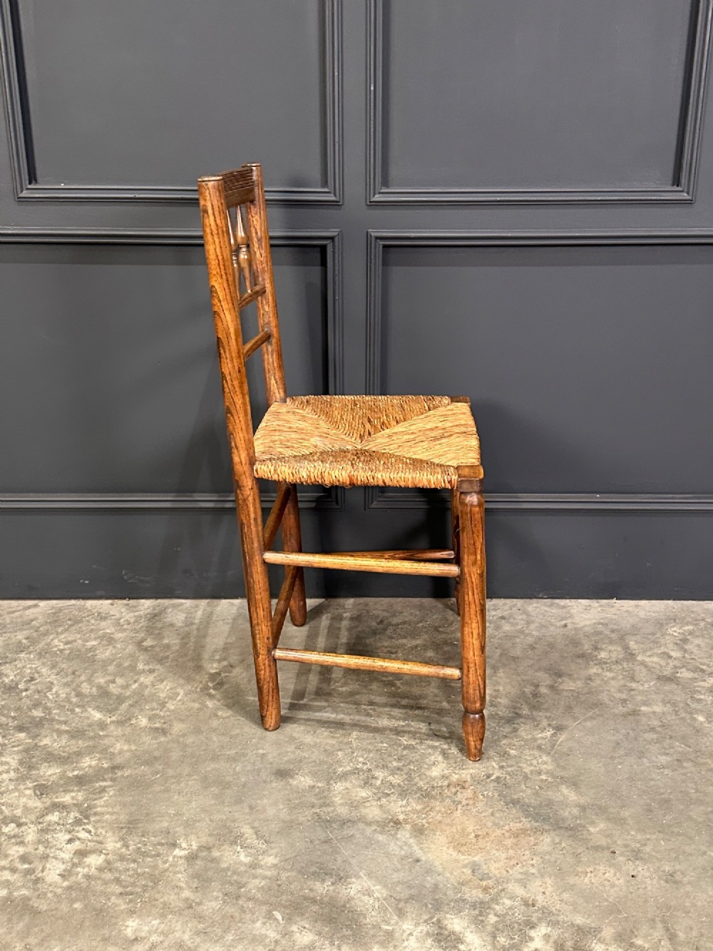 An 18th-century country elm side chair featuring a woven rush seat, turned spindle backrest, and turned wood legs connected by stretchers. View IX