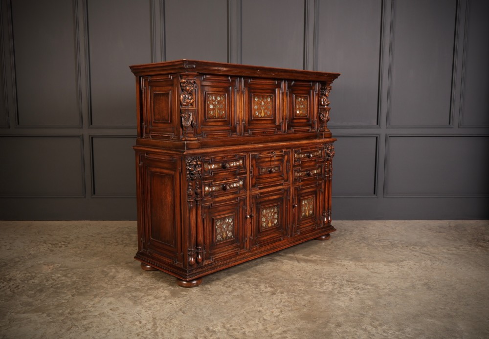 A two-tiered dark walnut sideboard featuring geometric mother of pearl inlays, hand-carved figurative relief accents, drawers, and panelled cabinet doors.