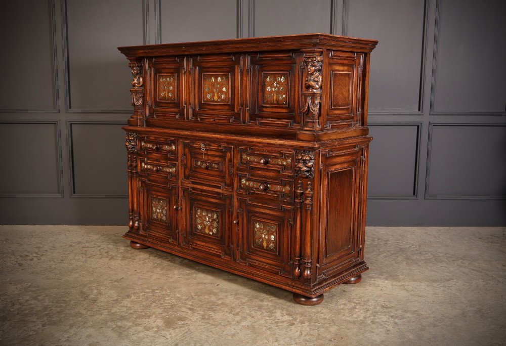 A two-tiered dark walnut sideboard featuring geometric mother of pearl inlays, hand-carved figurative relief accents, drawers, and panelled cabinet doors. View VII
