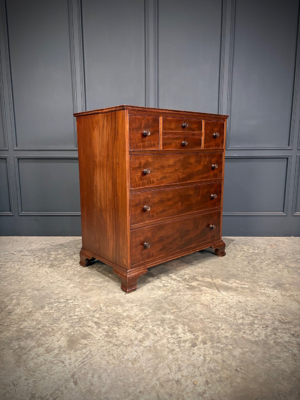 A tall antique mahogany chest of drawers featuring an upper arrangement of small drawers over three graduated full-width drawers, resting on bracket feet.