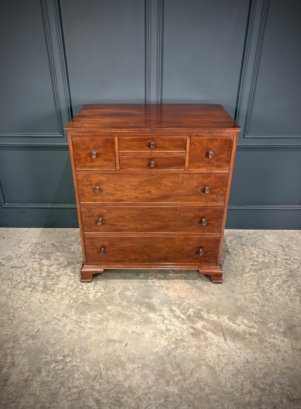 A tall antique mahogany chest of drawers featuring an upper arrangement of small drawers over three graduated full-width drawers, resting on bracket feet. View III