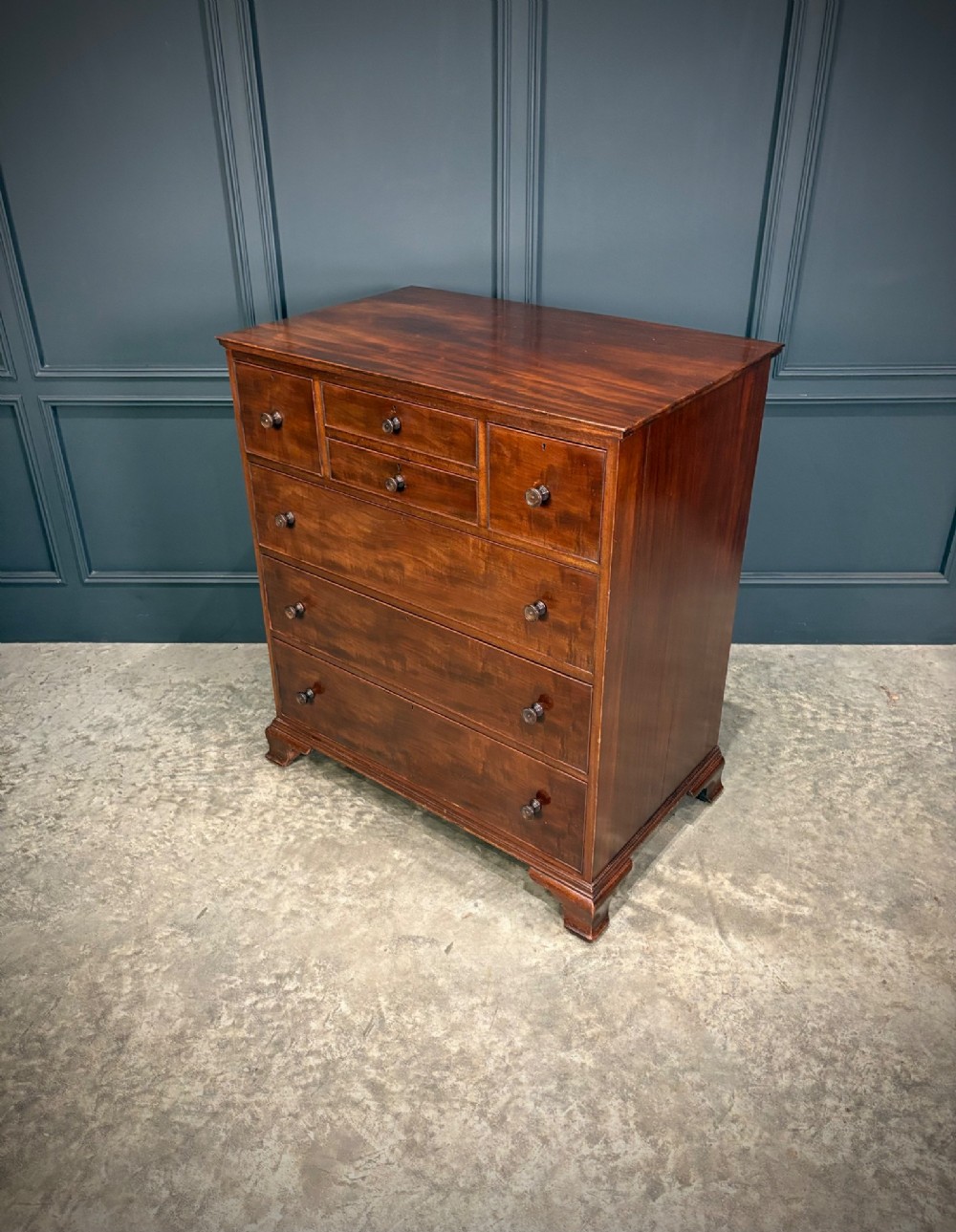 A tall antique mahogany chest of drawers featuring an upper arrangement of small drawers over three graduated full-width drawers, resting on bracket feet. View X