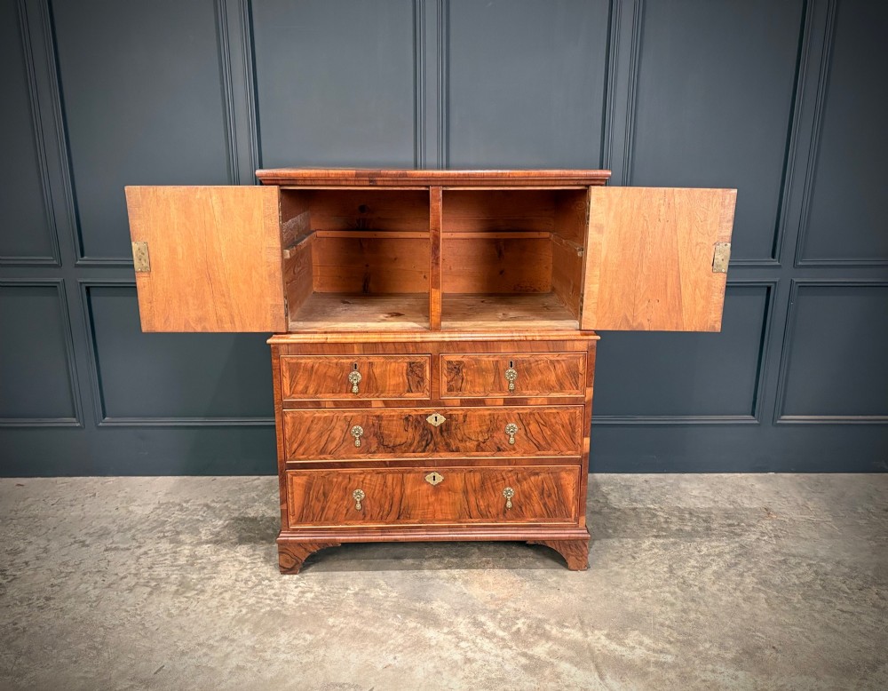 An antique walnut cabinet on chest featuring a twin-door top cupboard over graduating drawers with brass hardware and bracket feet. View VI