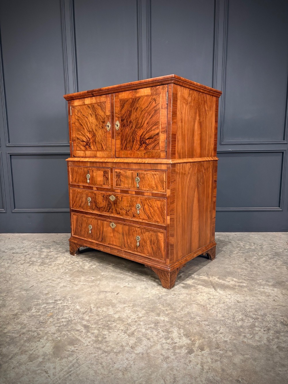 An antique walnut cabinet on chest featuring a twin-door top cupboard over graduating drawers with brass hardware and bracket feet.