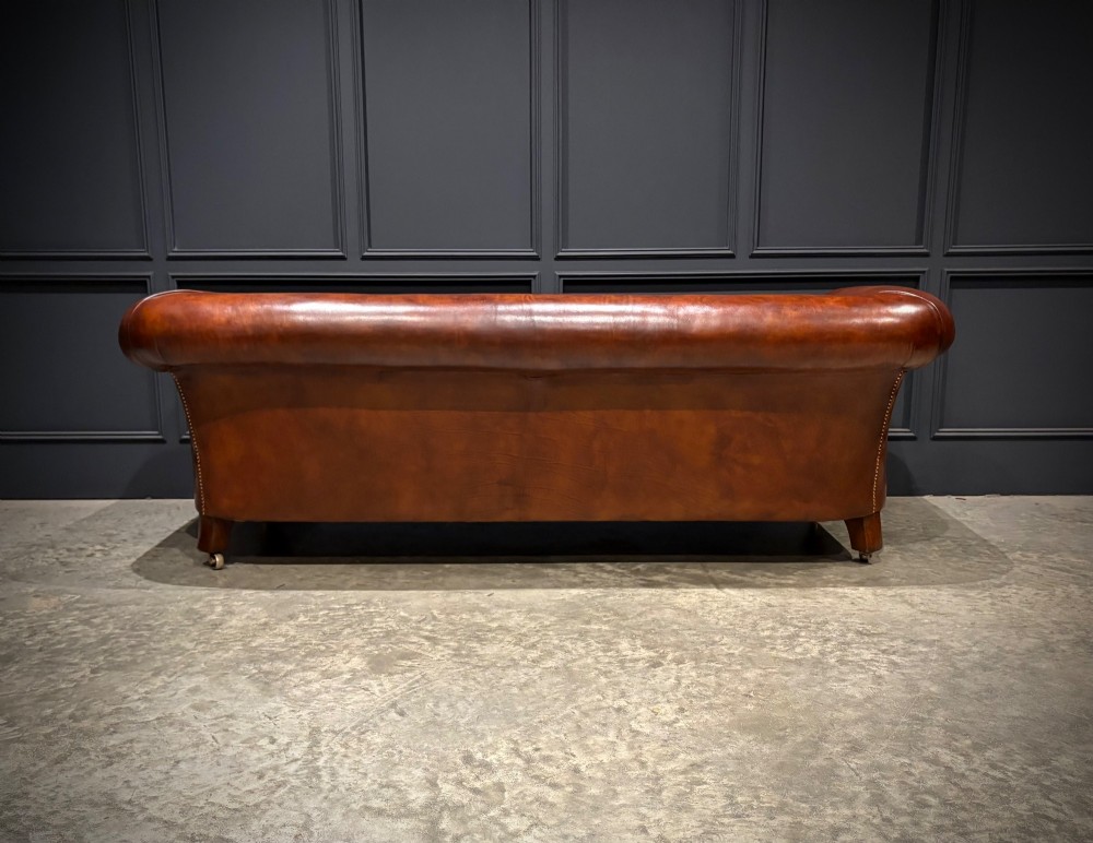 A Victorian chestnut brown leather sofa featuring continuous rolled arms, brass studding detail, and turned wood legs on castors. View XI