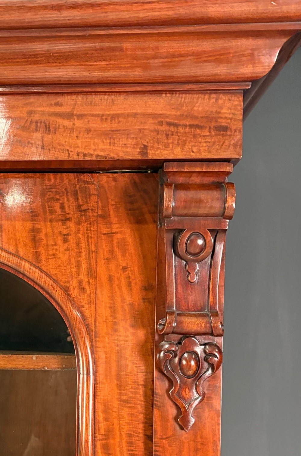 A large Victorian mahogany bookcase featuring two arched glazed doors, carved corbels, internal wooden shelves, and two drawers at the base. View III