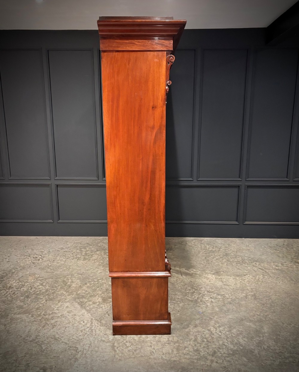 A large Victorian mahogany bookcase featuring two arched glazed doors, carved corbels, internal wooden shelves, and two drawers at the base. View VIII