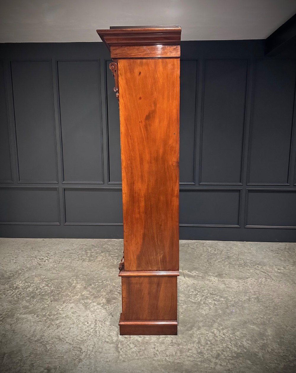 A large Victorian mahogany bookcase featuring two arched glazed doors, carved corbels, internal wooden shelves, and two drawers at the base. View XI