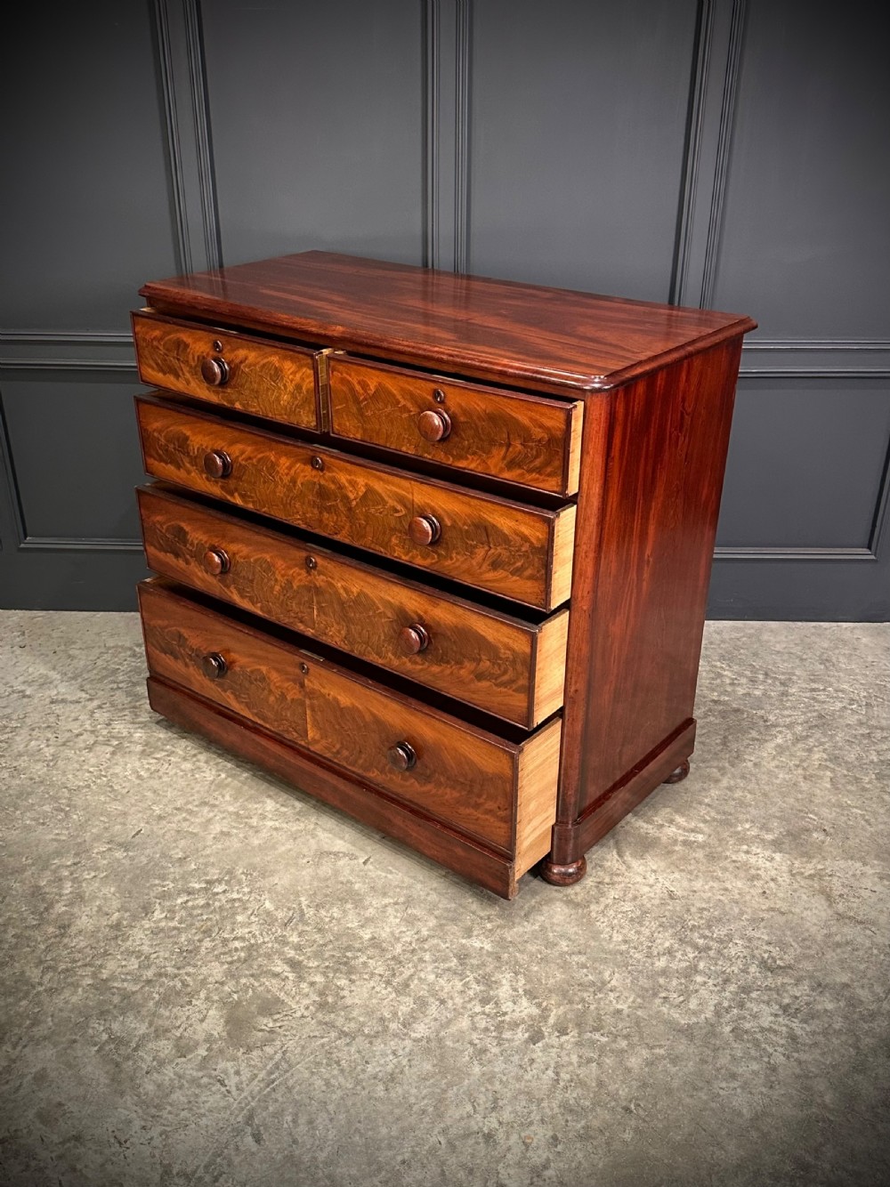 A Victorian mahogany chest of drawers featuring a two short over three long drawer arrangement with turned wood handles and flame mahogany grain patterns. View V
