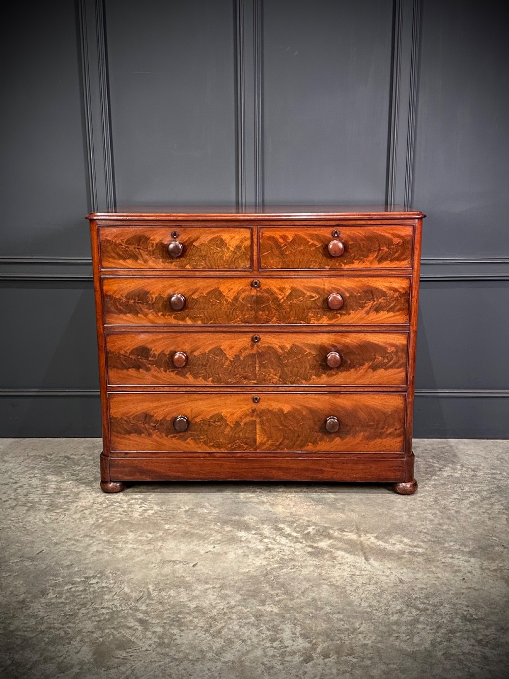 A Victorian mahogany chest of drawers featuring a two short over three long drawer arrangement with turned wood handles and flame mahogany grain patterns.
