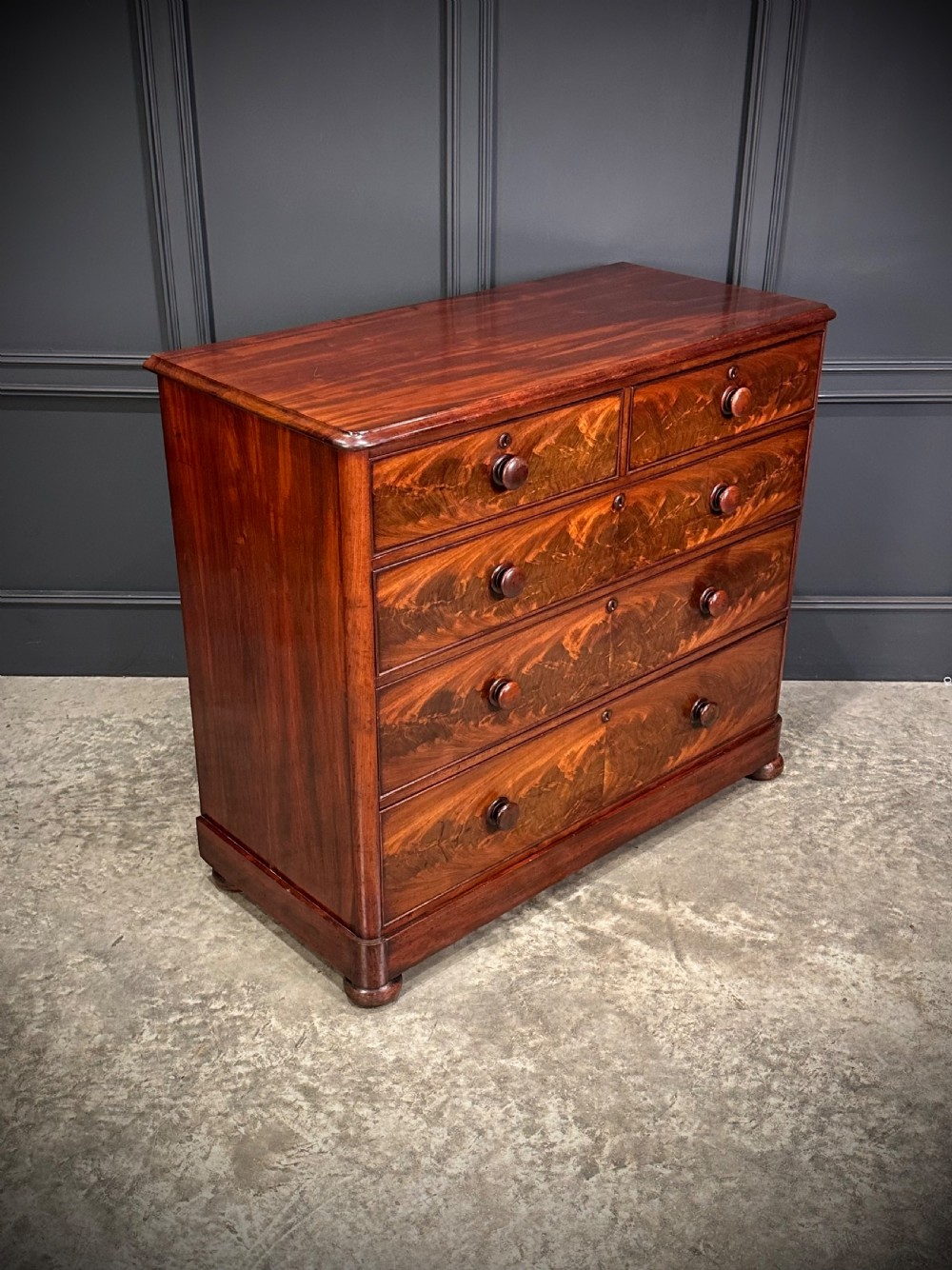 A Victorian mahogany chest of drawers featuring a two short over three long drawer arrangement with turned wood handles and flame mahogany grain patterns. View VIII