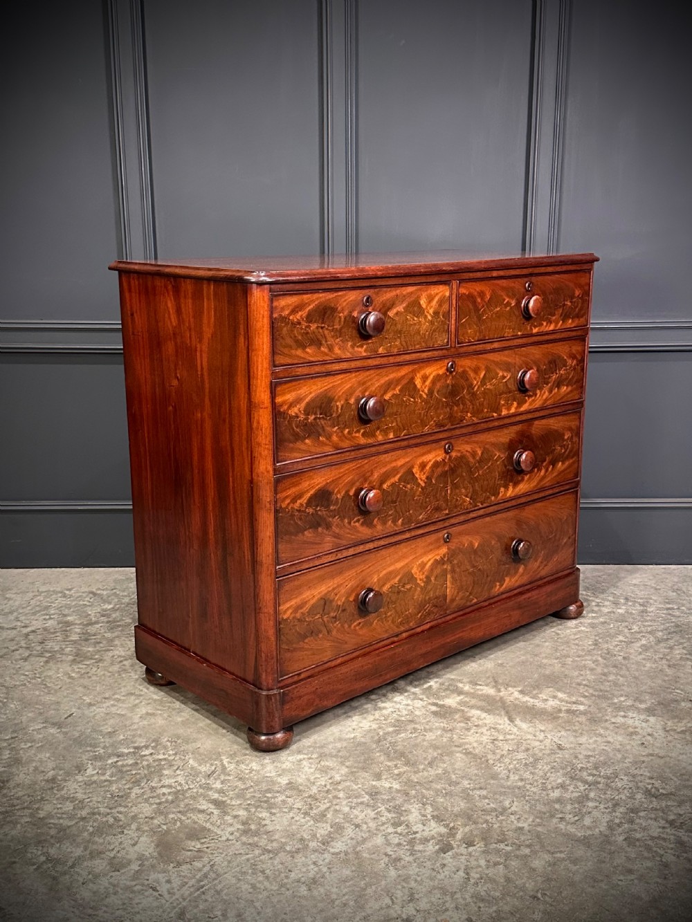 A Victorian mahogany chest of drawers featuring a two short over three long drawer arrangement with turned wood handles and flame mahogany grain patterns. View IX