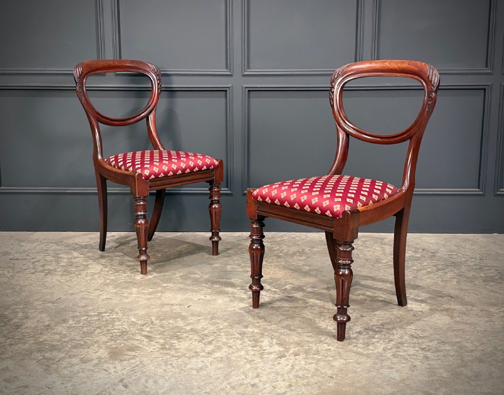 A pair of Victorian mahogany side chairs with rounded balloon backs, turned front legs, and red patterned fabric seats.