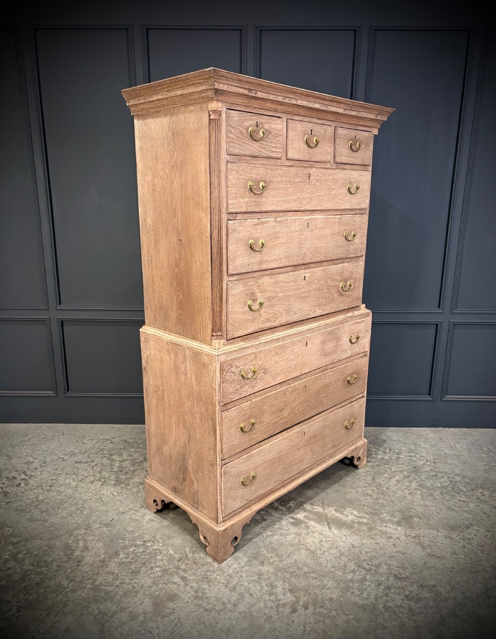 A Georgian bleached oak chest on chest featuring a two-part stacked design with brass drop handles and bracket feet.
