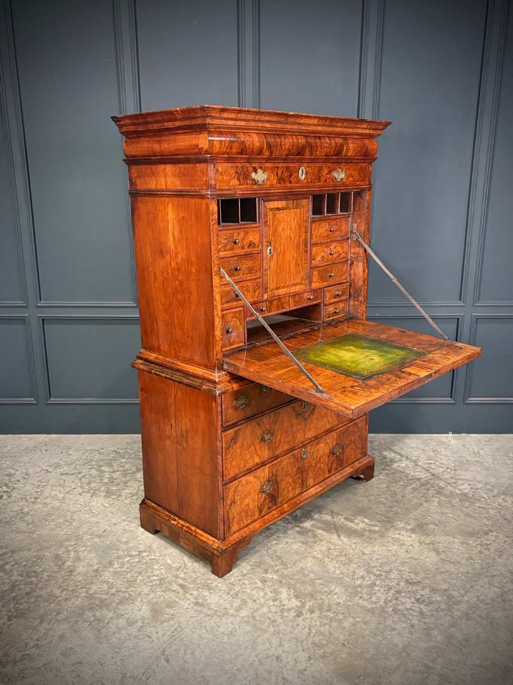 An antique Queen Anne walnut escritoire featuring a drop-front writing surface revealing a fitted interior above a base with drawers.