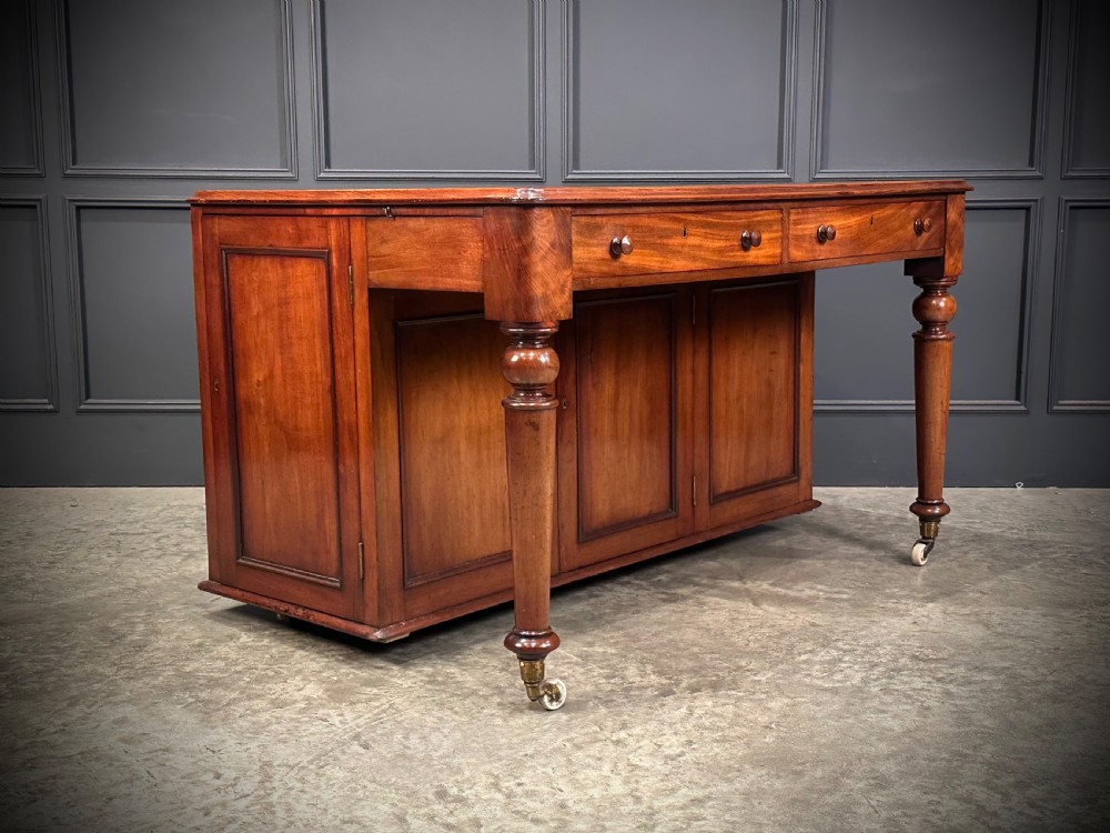A Victorian mahogany writing desk featuring a green leather inset top, frieze drawers, turned legs on brass castors, and lower panelled cabinet doors. View III