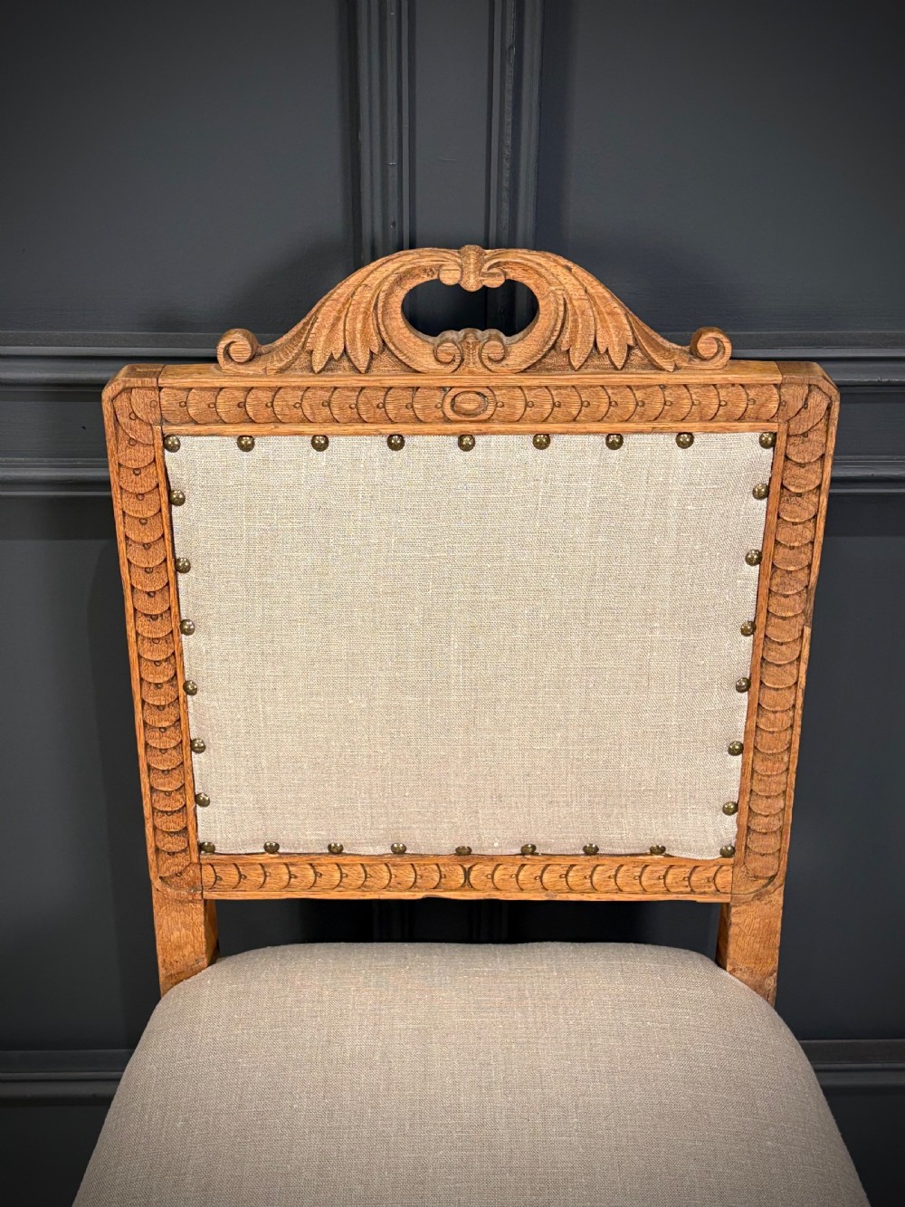 A set of six carved bleached oak dining chairs upholstered in neutral linen fabric with brass stud trimming and turned front legs on ceramic castors. View V