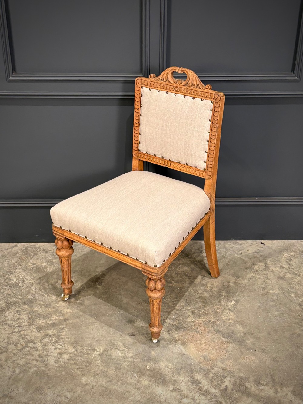 A set of six carved bleached oak dining chairs upholstered in neutral linen fabric with brass stud trimming and turned front legs on ceramic castors. View VII