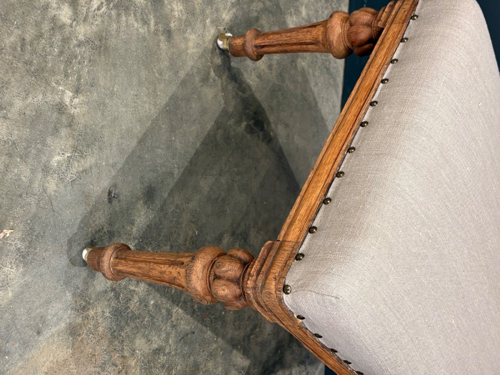 A set of six carved bleached oak dining chairs upholstered in neutral linen fabric with brass stud trimming and turned front legs on ceramic castors. View VIII