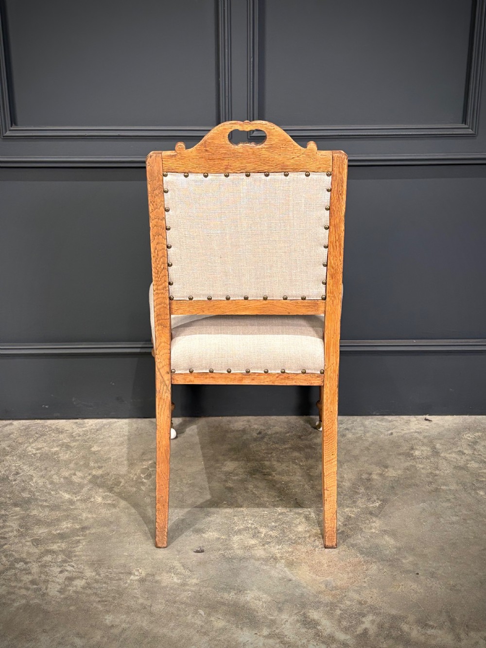 A set of six carved bleached oak dining chairs upholstered in neutral linen fabric with brass stud trimming and turned front legs on ceramic castors. View XI