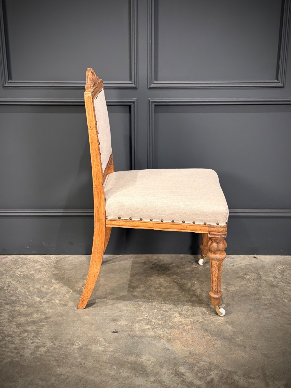 A set of six carved bleached oak dining chairs upholstered in neutral linen fabric with brass stud trimming and turned front legs on ceramic castors. View XII