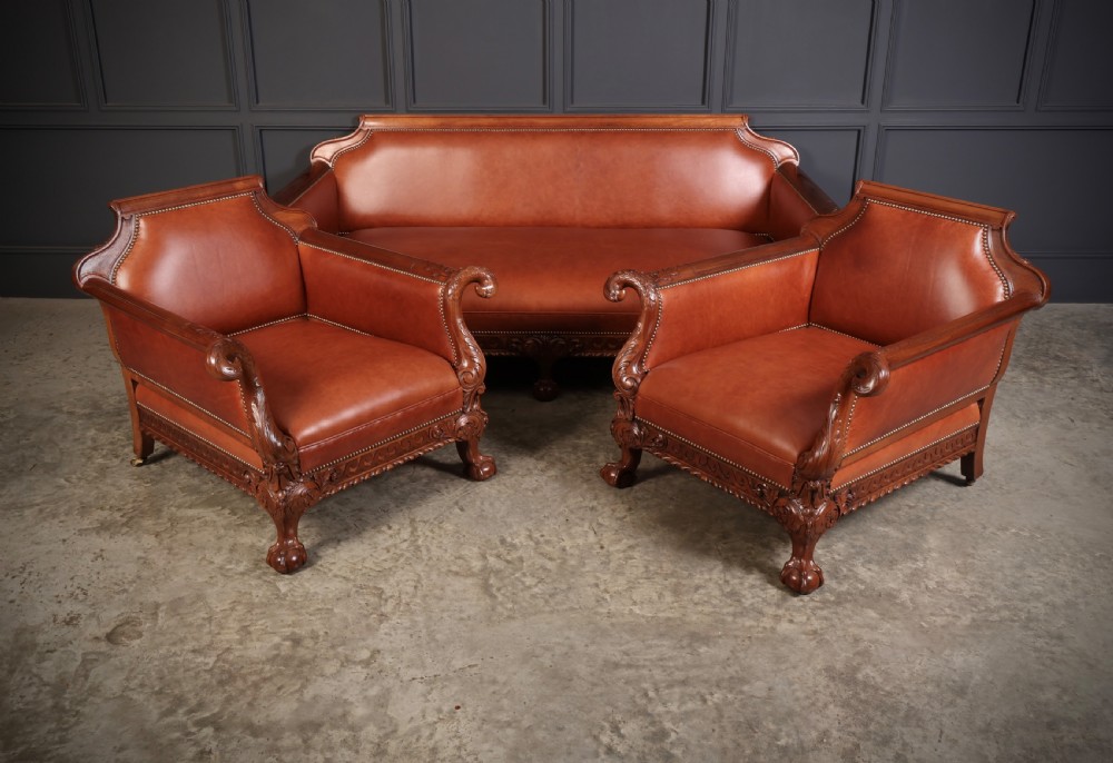 A three-piece lounge suite comprising a three-seater sofa and two matching armchairs upholstered in chestnut brown leather with carved mahogany frames and claw and ball feet.
