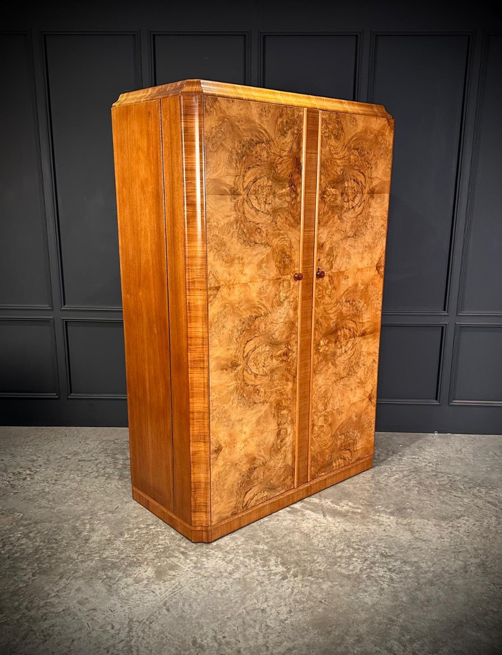 An Art Deco twin-door wardrobe crafted from figured burr walnut veneer with rounded top edges and dark circular handles.