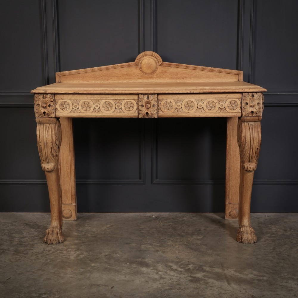A carved bleached oak console table featuring a raised back gallery, rosette carved frieze, and sculptural monopodium legs terminating in lion paw feet.
