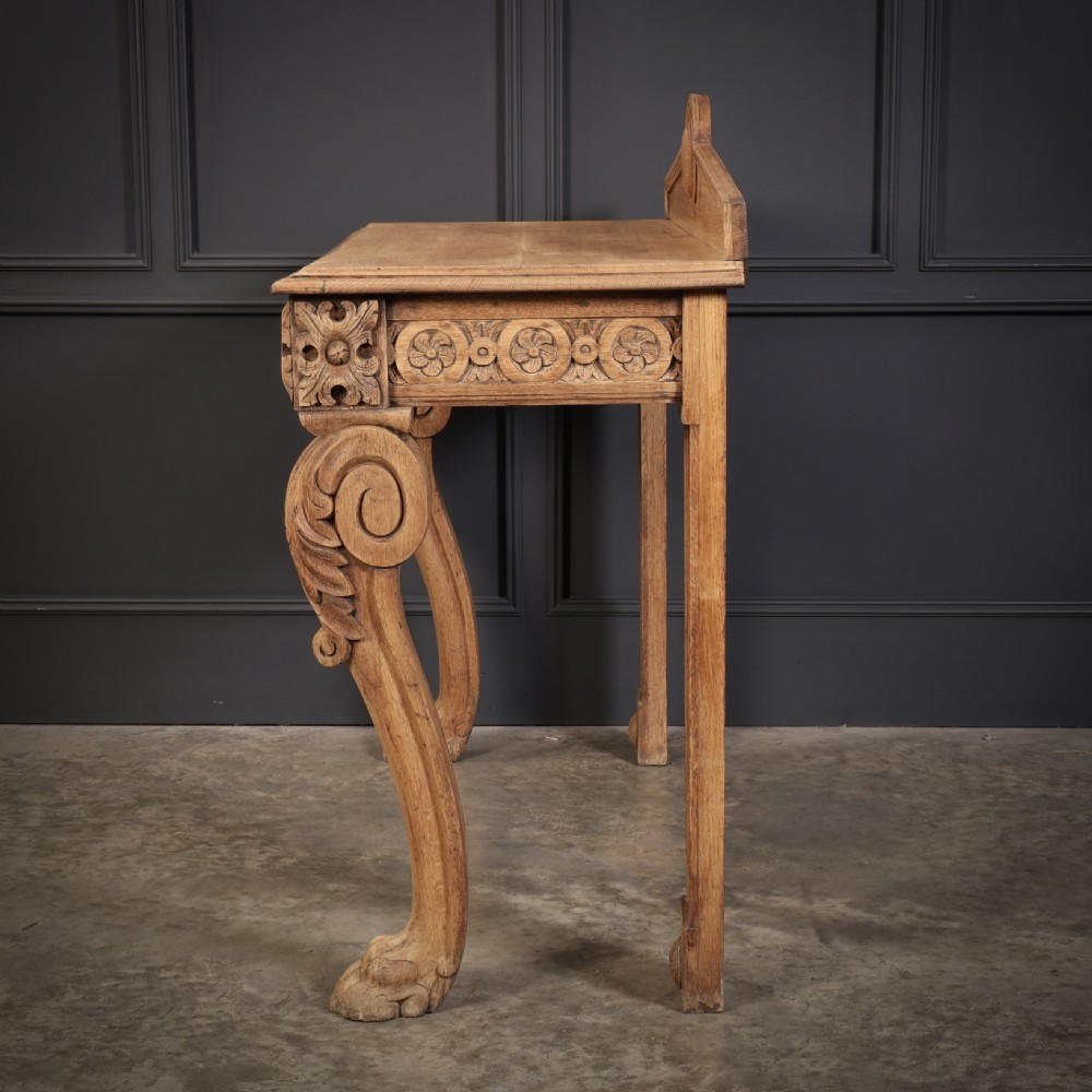A carved bleached oak console table featuring a raised back gallery, rosette carved frieze, and sculptural monopodium legs terminating in lion paw feet. View XIII