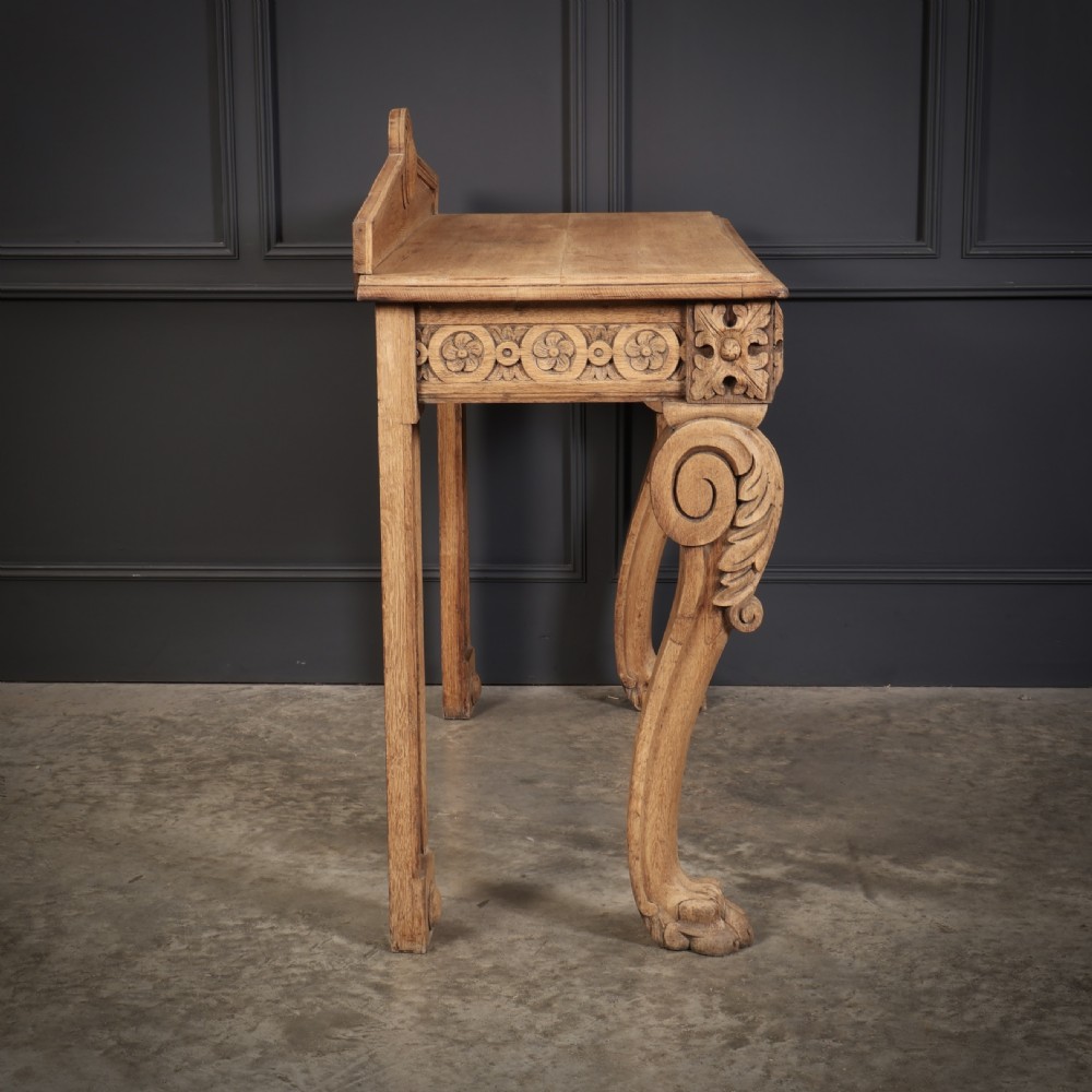 A carved bleached oak console table featuring a raised back gallery, rosette carved frieze, and sculptural monopodium legs terminating in lion paw feet. View XV