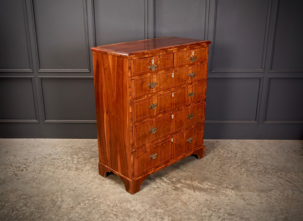 A Georgian walnut chest of drawers with figured grain, brass drop handles, bone escutcheons, and bracket feet. View III