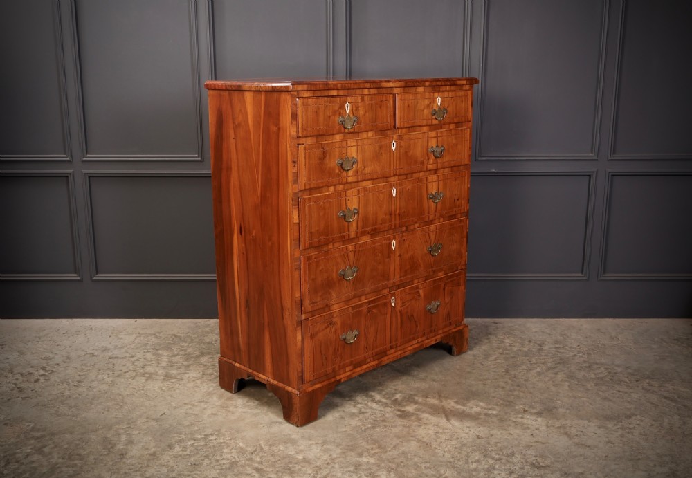 A Georgian walnut chest of drawers with figured grain, brass drop handles, bone escutcheons, and bracket feet. View II