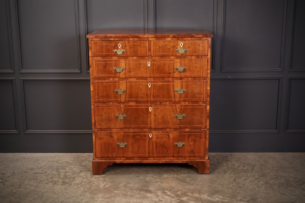 A Georgian walnut chest of drawers with figured grain, brass drop handles, bone escutcheons, and bracket feet.