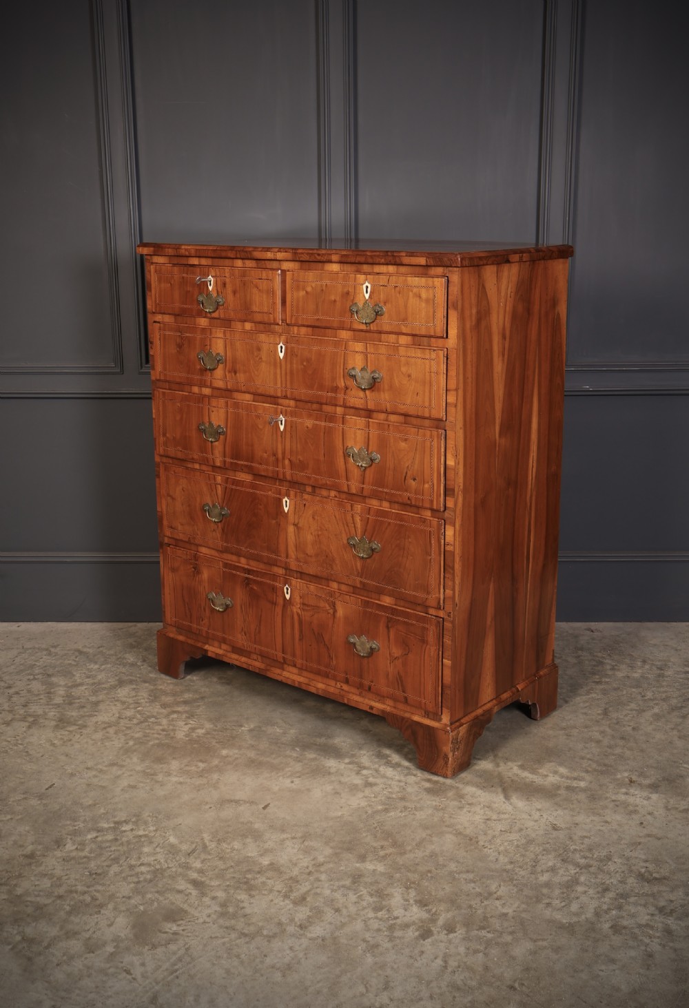 A Georgian walnut chest of drawers with figured grain, brass drop handles, bone escutcheons, and bracket feet. View V