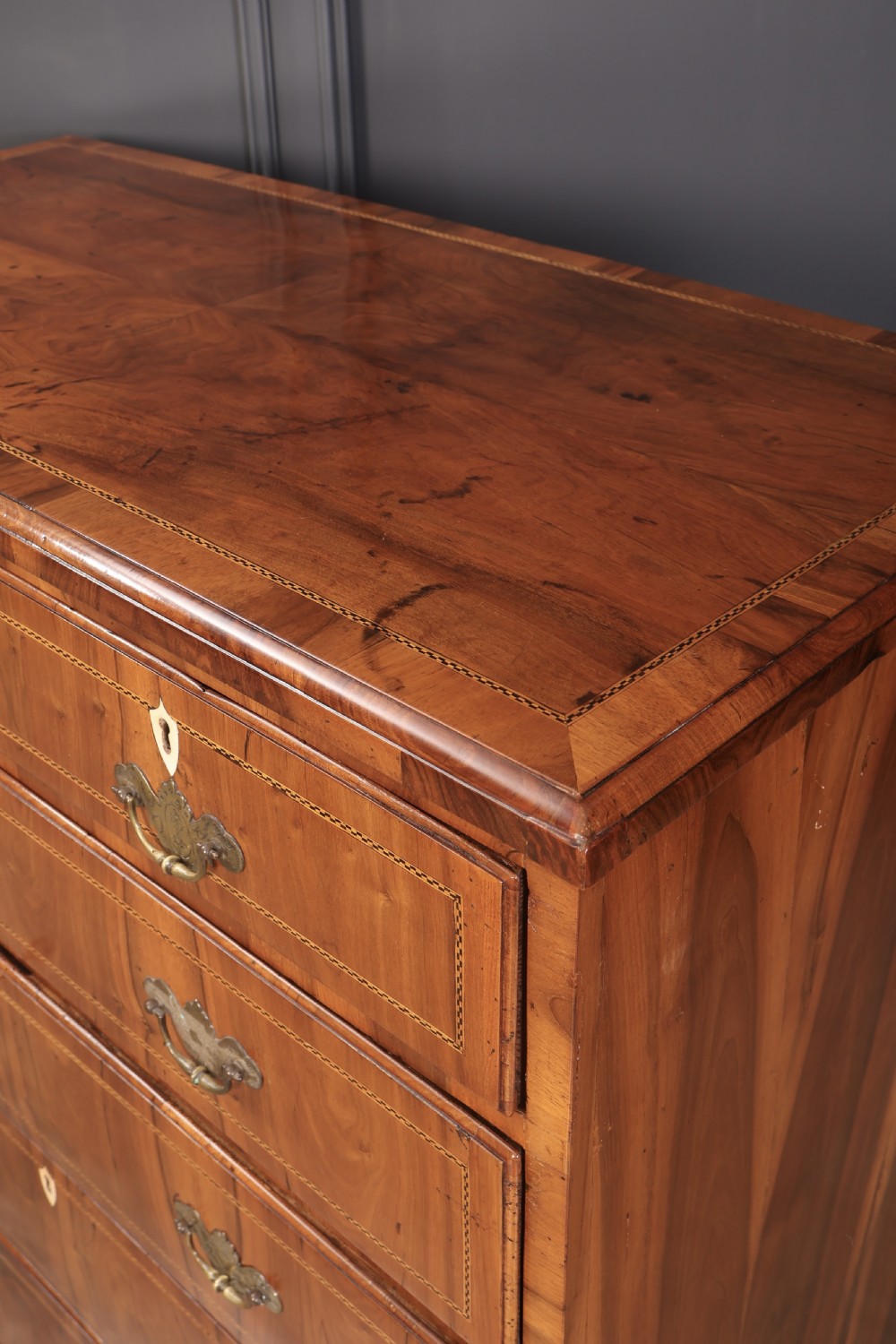 A Georgian walnut chest of drawers with figured grain, brass drop handles, bone escutcheons, and bracket feet. View VI