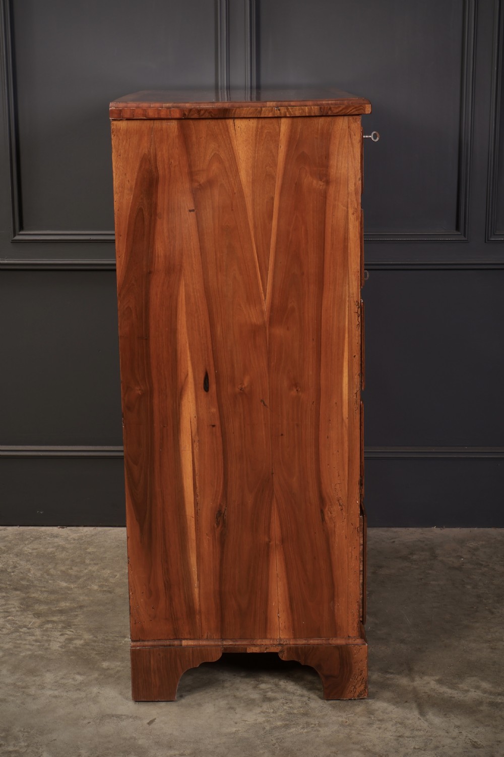 A Georgian walnut chest of drawers with figured grain, brass drop handles, bone escutcheons, and bracket feet. View X